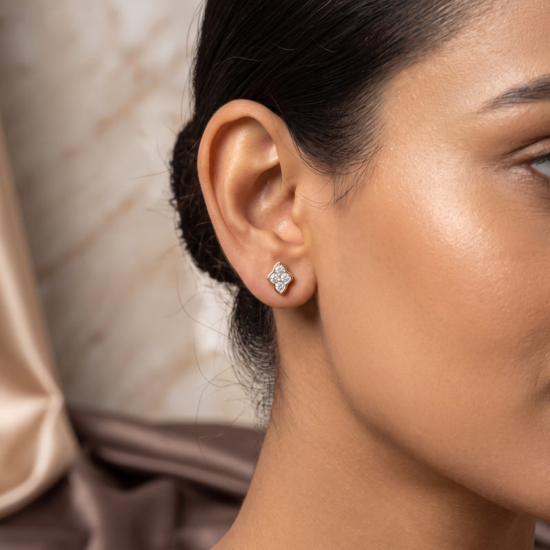 A close-up side profile of a woman wearing a small diamond-shaped stud earring with a silver-toned setting and clear stones.