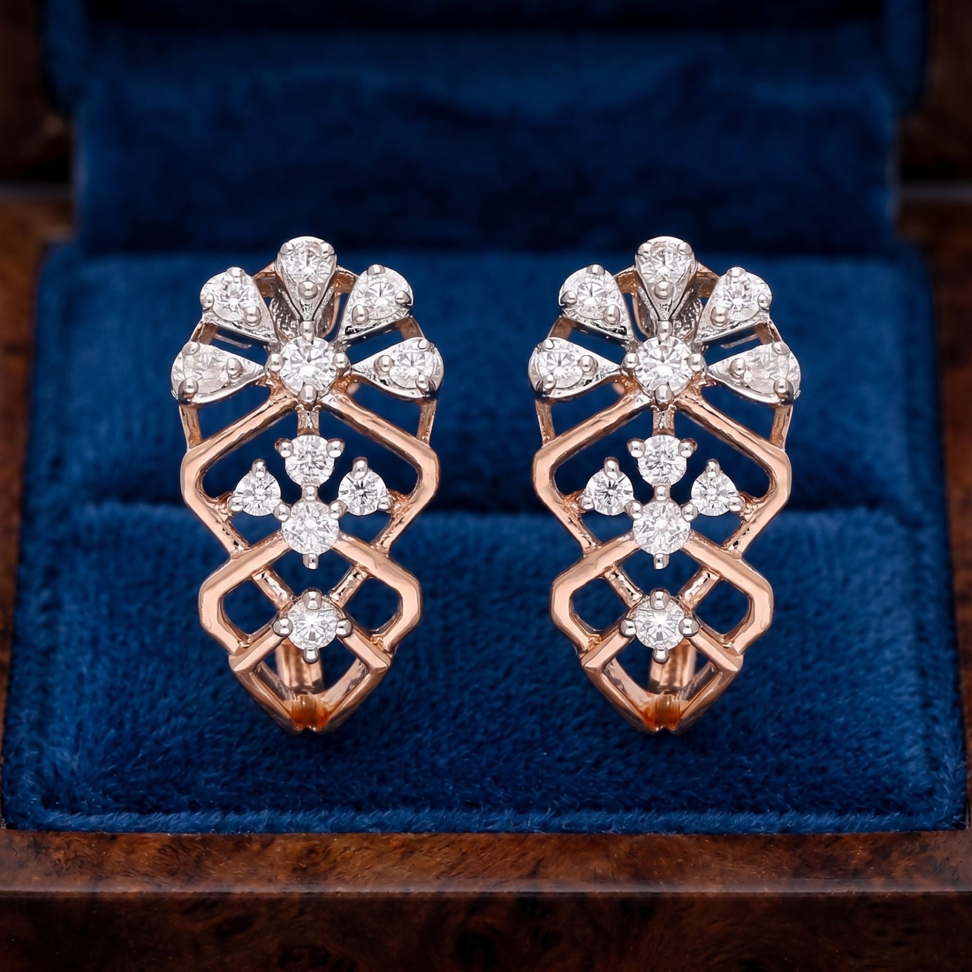 Pair of rose gold and diamond earrings on a blue cushion