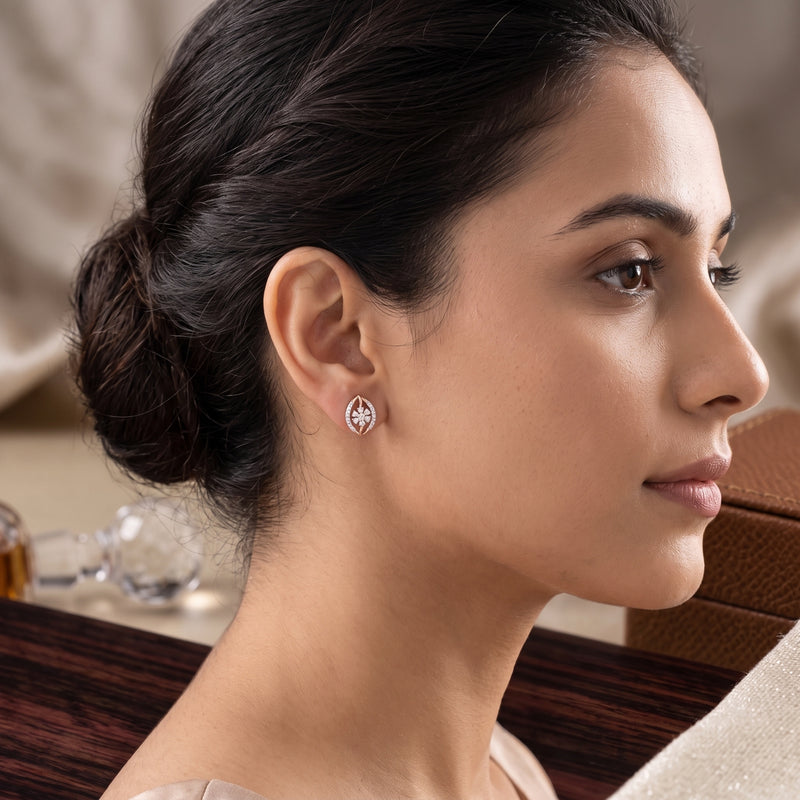 A close-up side profile of a woman wearing a small geometric stud earring in a warm indoor setting.