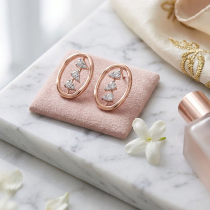 Rose gold earrings on a pink cushion with a marble surface and flowers.