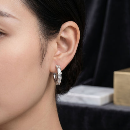 Close-up of a person wearing diamond hoop earrings with a blurred background