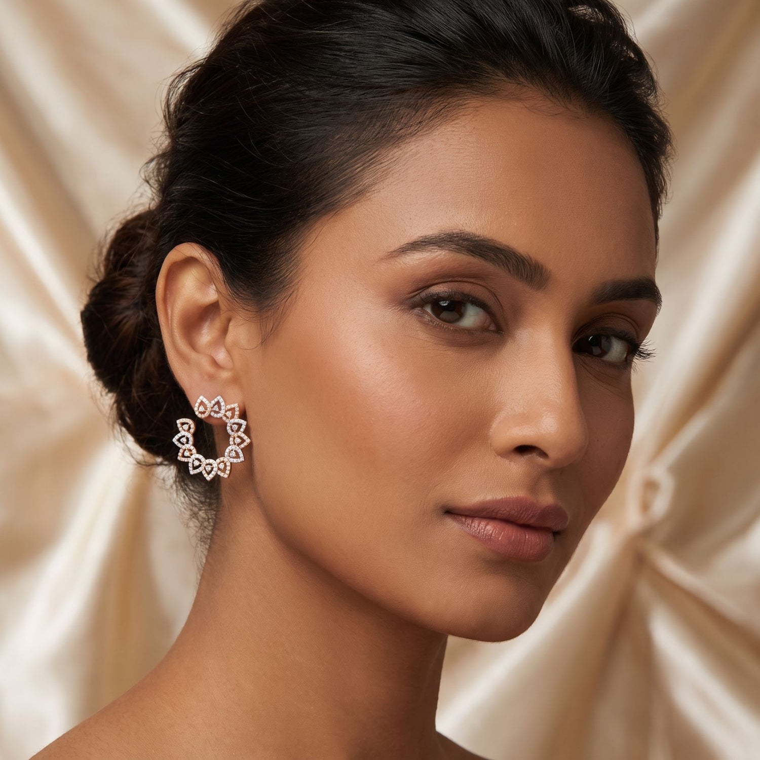 Woman wearing a pair of hoop earrings against a beige fabric background