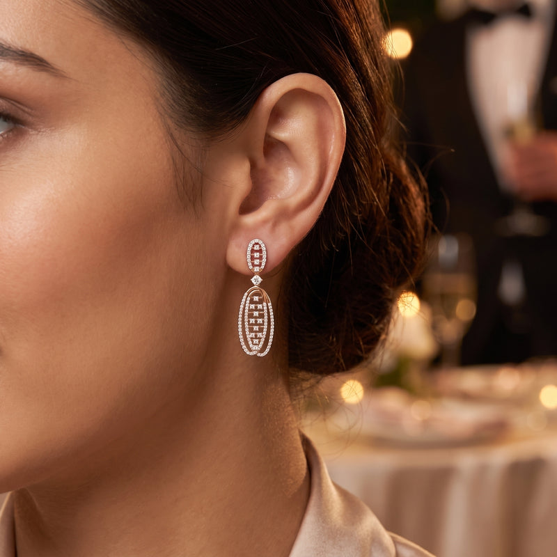 A close-up lifestyle shot of a woman wearing a delicate, multi-stone drop earring in a warm, elegant indoor setting with soft bokeh lights in the background.