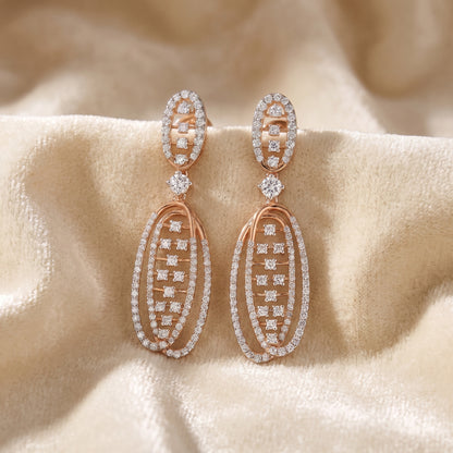 Rose gold drop earrings with multiple rows of clear pavé-set stones, displayed on a soft beige satin fabric background.