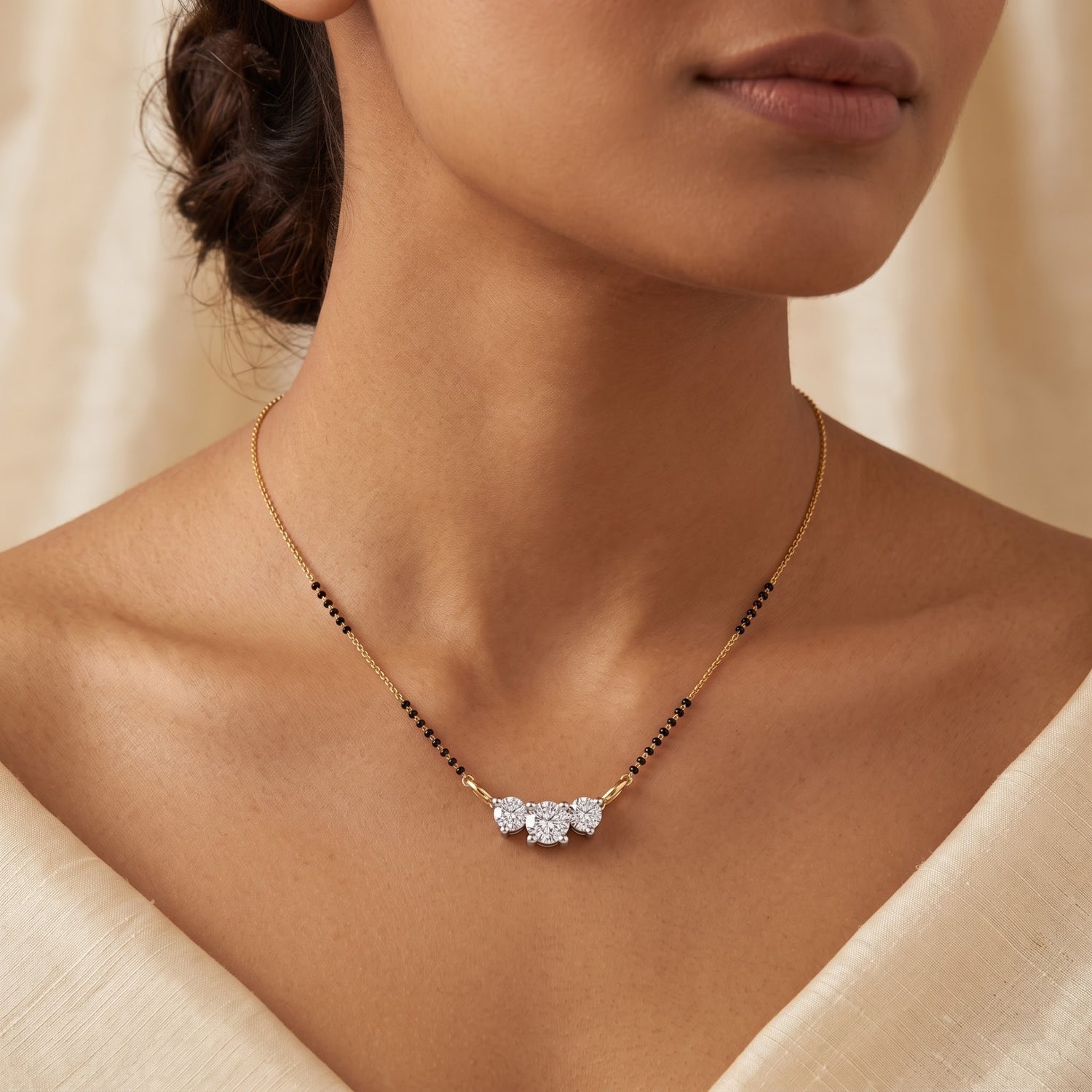 A close-up of a model wearing a delicate gold chain necklace with a small bow-shaped cluster of clear stones at the center and small black bead accents along the chain.