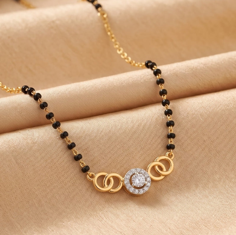 A gold and black beaded necklace with a central circular pendant featuring a clear stone, displayed on a beige satin fabric background.
