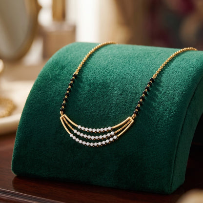 A gold necklace with three curved rows of white pearls and small black beads, displayed on a green velvet jewelry stand.
