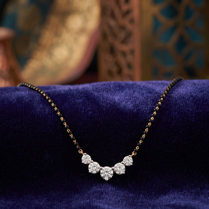 A delicate necklace with a small cluster of clear stones on a fine gold-toned chain, displayed on a deep blue velvet surface with a softly blurred ornate background.