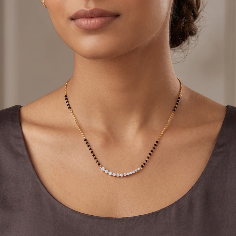 A close-up of a model wearing a delicate necklace with a curved row of small white stones set on a gold chain, accented with small black beads.