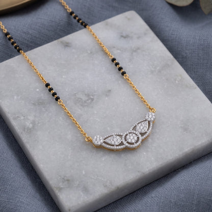 A gold and white gold necklace with a beaded black chain and a curved pavé pendant, displayed on a white marble block over a textured gray fabric background.