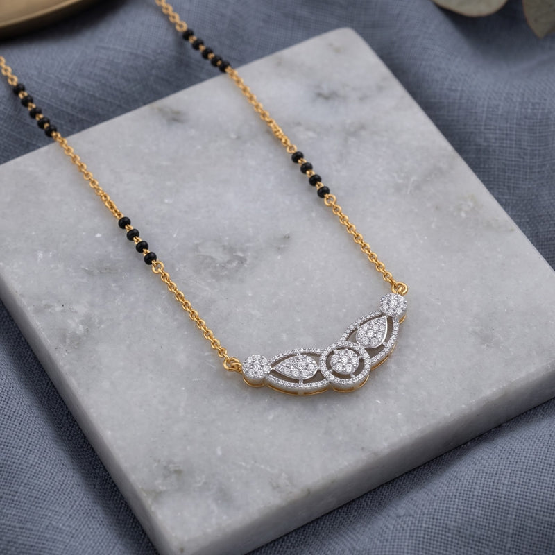 A gold and white gold necklace with a beaded black chain and a curved pavé pendant, displayed on a white marble block over a textured gray fabric background.