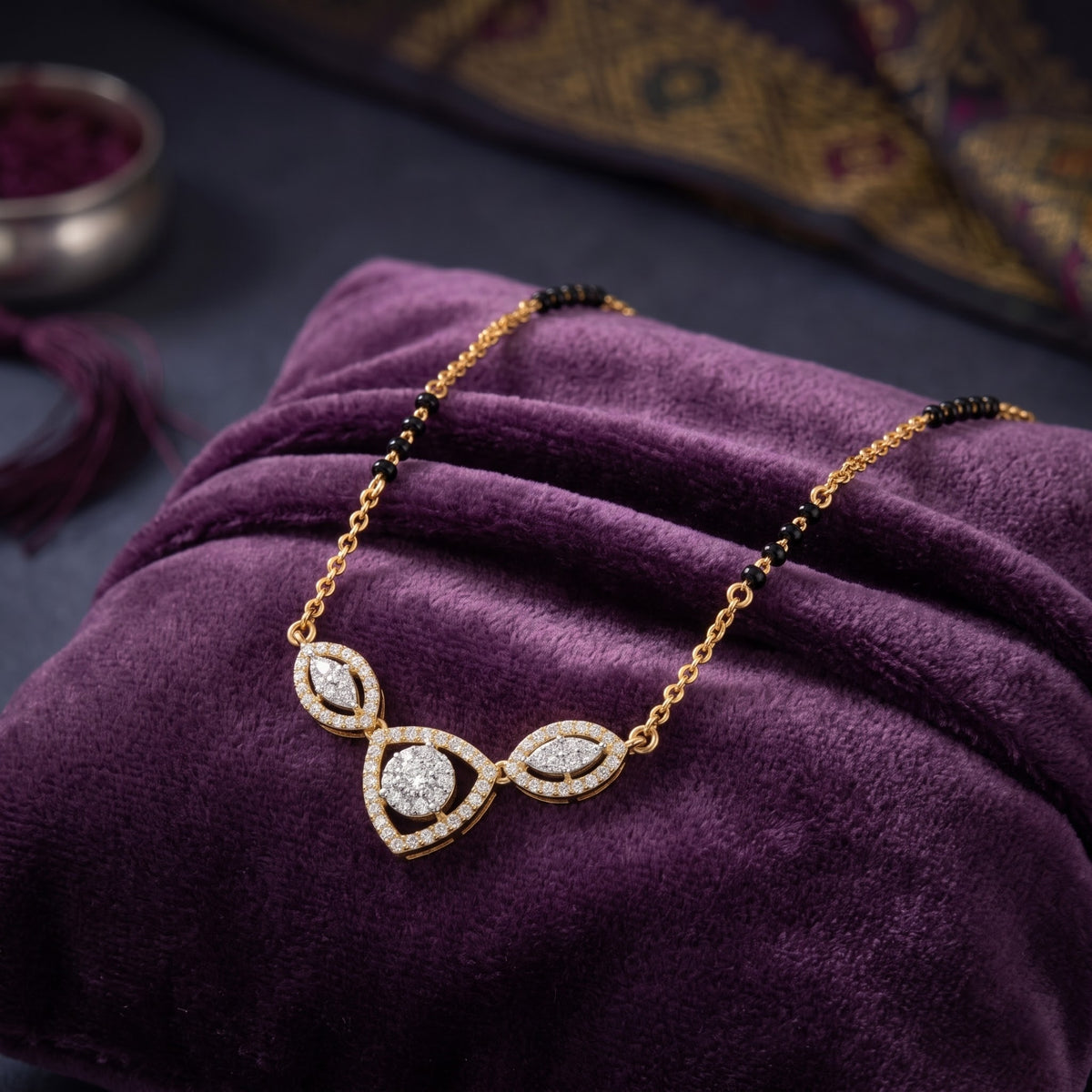 Gold necklace with a pavé-set teardrop pendant and small black beads, displayed on a purple velvet fabric background.