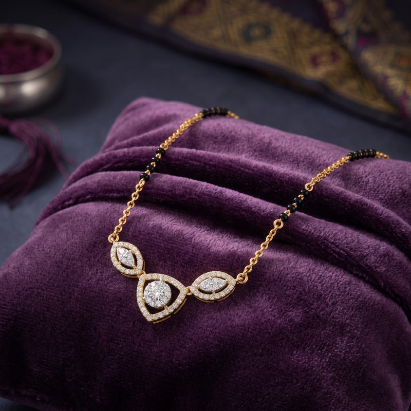 Gold necklace with a pavé-set teardrop pendant and small black beads, displayed on a purple velvet fabric background.
