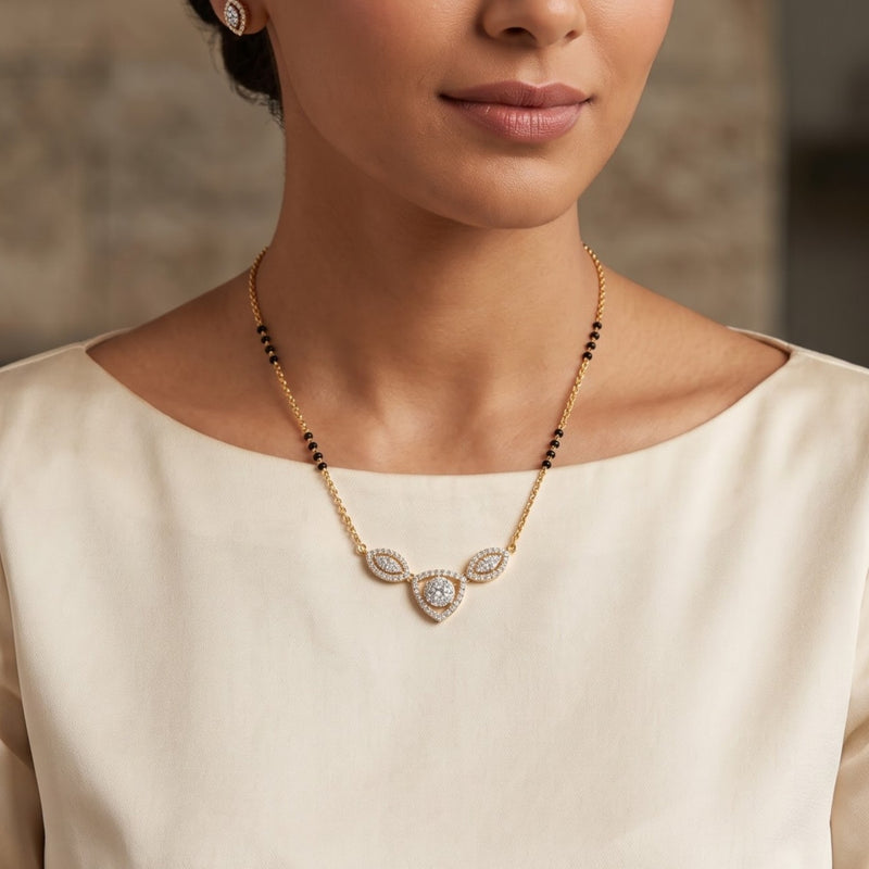 A close-up of a model wearing a delicate gold necklace with a V-shaped pendant featuring clear stones and small black beads along the chain, paired with a cream-colored top.
