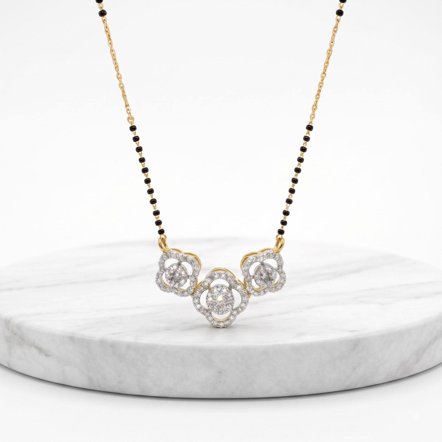 A delicate gold and black beaded necklace with a central cluster of clear gemstones, displayed on a round white marble pedestal against a clean white background.