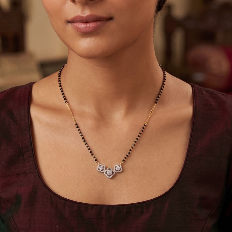 A close-up of a woman wearing a traditional Indian black bead necklace with a gold chain and a silver-toned floral pendant.