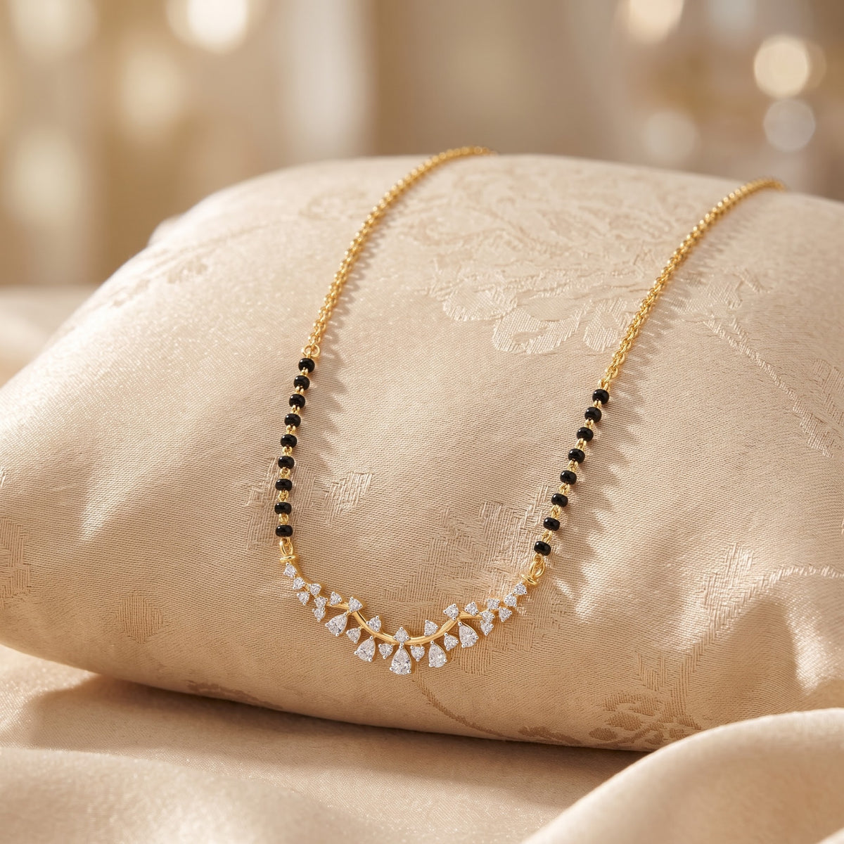 A gold chain necklace with a curved V-shaped pendant featuring small clear stones and alternating rows of black and white stones, displayed on a beige satin cushion.