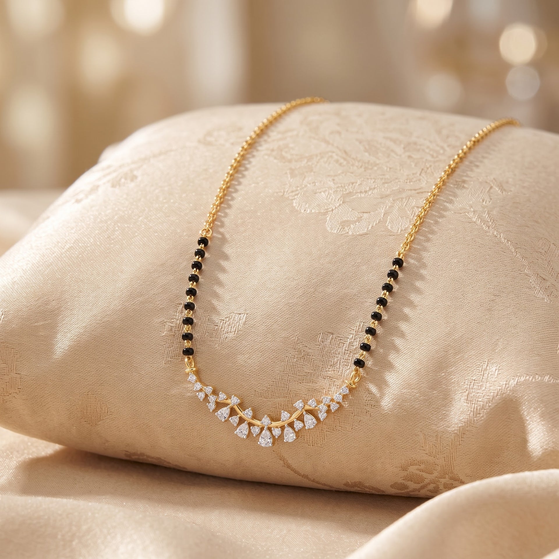 A gold chain necklace with a curved V-shaped pendant featuring small clear stones and alternating rows of black and white stones, displayed on a beige satin cushion.
