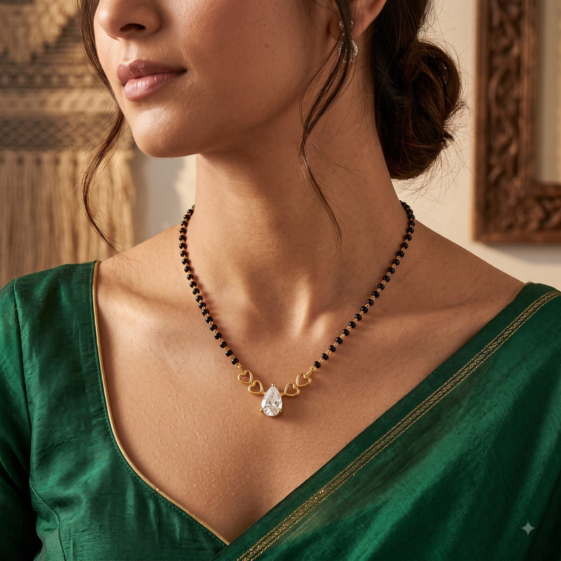 A close-up of a woman wearing a beaded necklace with a gold-toned leaf motif and a clear teardrop-shaped stone pendant, paired with a green blouse.
