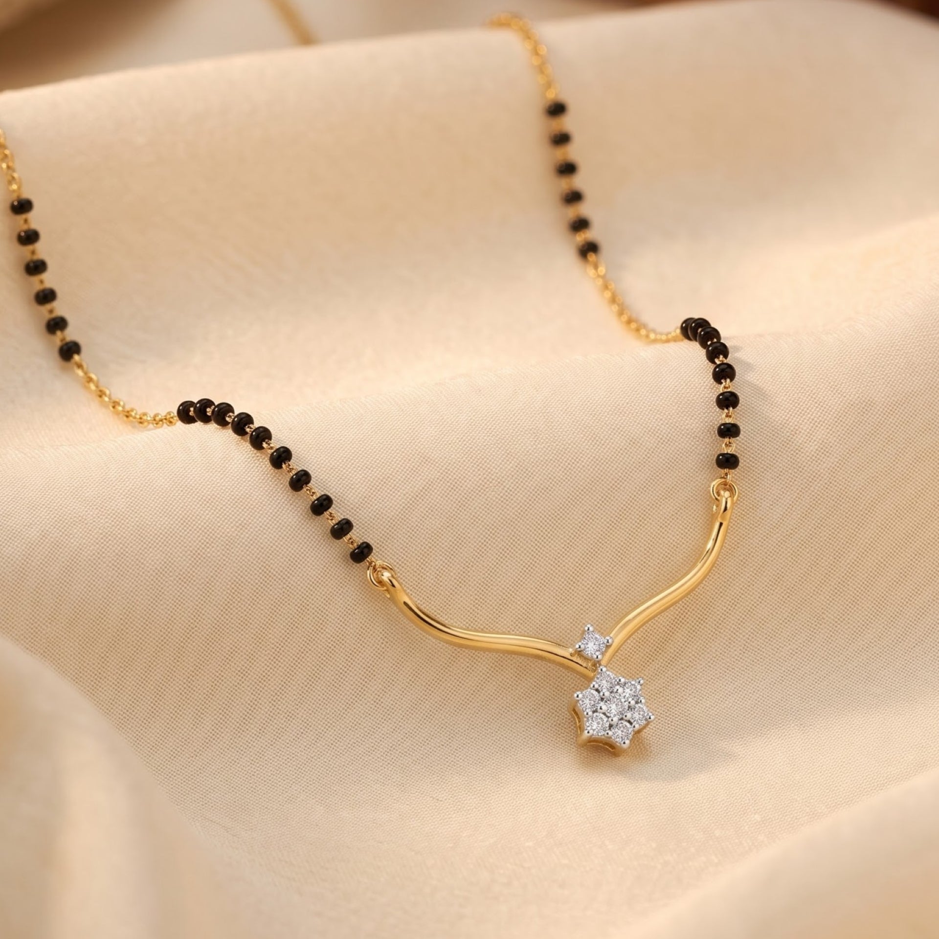 A gold and black beaded necklace with a curved gold pendant and a clear crystal flower setting, displayed on draped beige fabric.