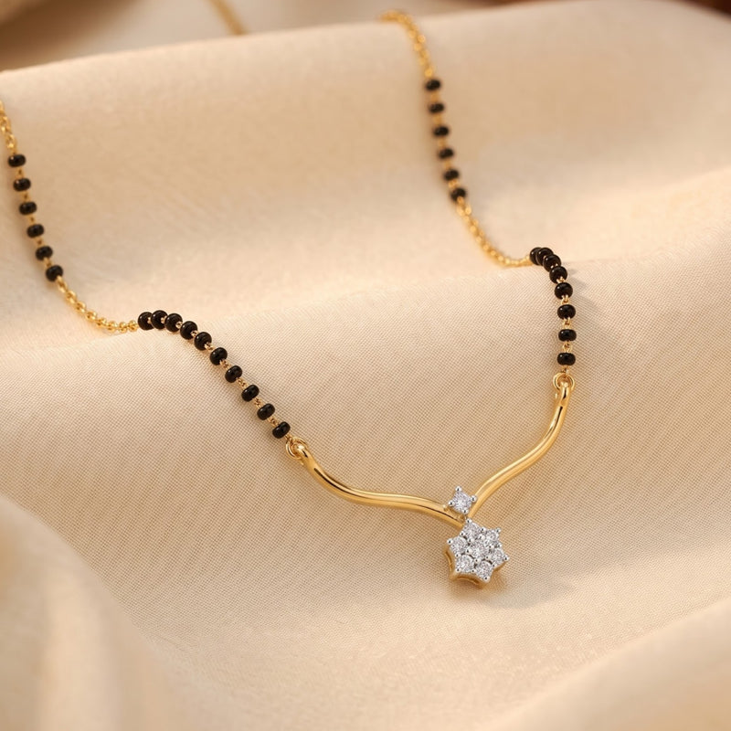 A gold and black beaded necklace with a curved gold pendant and a clear crystal flower setting, displayed on draped beige fabric.
