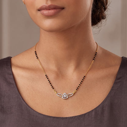 A close-up of a woman wearing a delicate gold necklace with a winged pendant featuring a teardrop-shaped clear stone, paired with black and gold beaded strands.