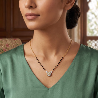 A close-up lifestyle shot of a model wearing a delicate gold necklace with a winged pendant featuring a central clear gemstone and small side stones, accented by a row of small black beads along the chain.