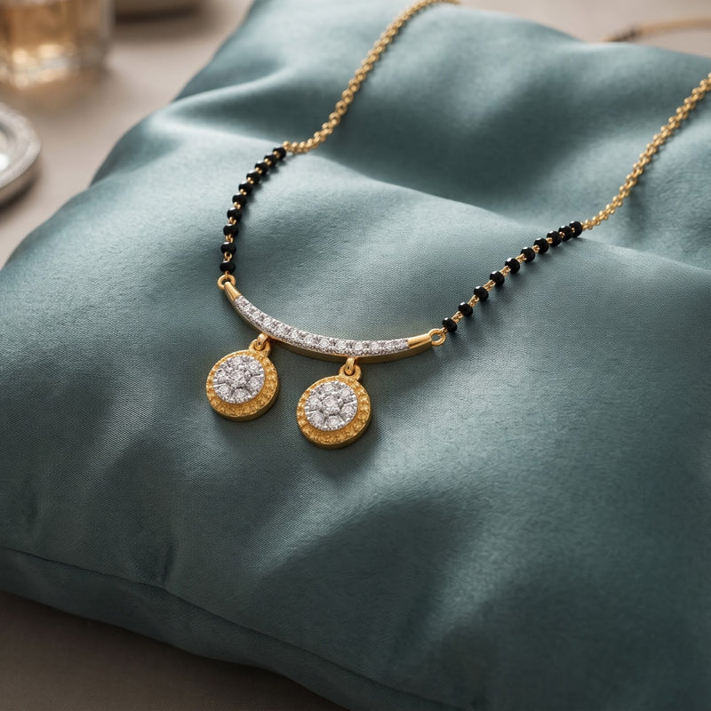 Gold-tone necklace with a curved bar set with small clear stones, black bead accents, and two round gold pendants with clear stones, displayed on a teal satin cushion.