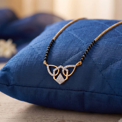 A gold and black beaded necklace with a heart-shaped pendant set with small clear stones, resting on a textured blue quilted cushion.