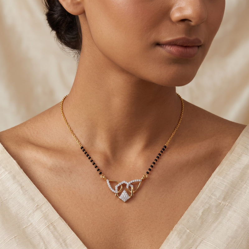 A close-up lifestyle shot of a model wearing a delicate gold chain necklace with a central pendant. The necklace features a gold chain accented with small black beads, and a central pendant composed of gold loops set with clear pavé stones.