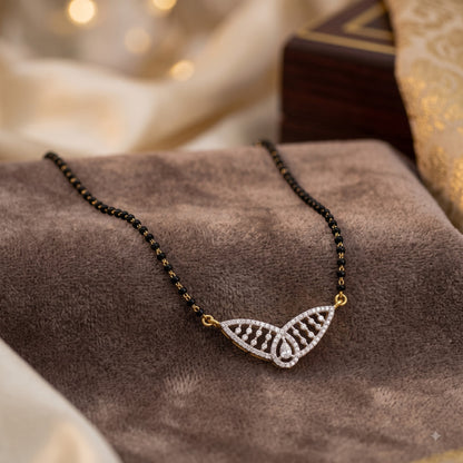 A delicate necklace with a black beaded chain and a butterfly-shaped pendant set with small clear stones and gold-tone accents, displayed on a brown velvet surface.