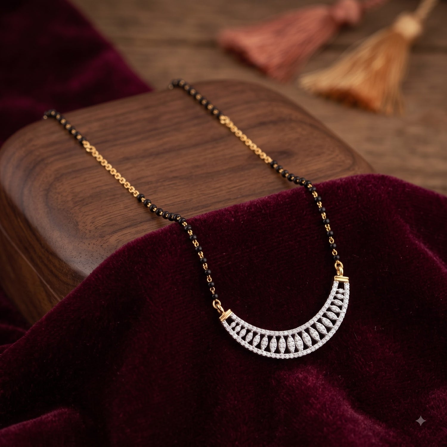 A gold and black beaded necklace with a silver crescent-shaped pendant set with clear stones, displayed on a dark wooden block draped with deep burgundy velvet.