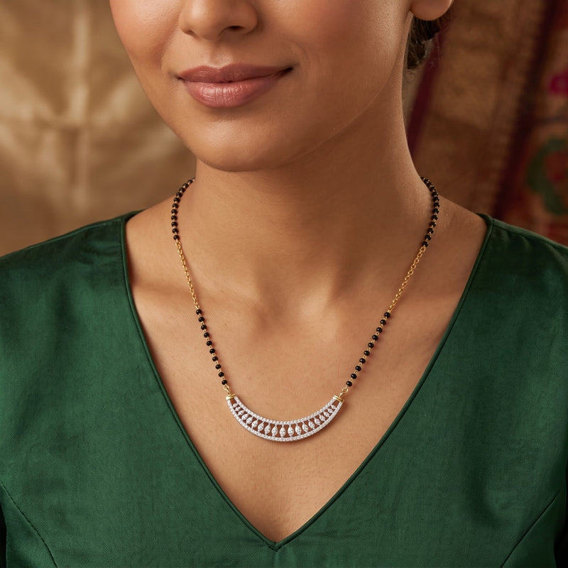 A close-up of a woman wearing a gold and silver crescent-shaped necklace with black beads, paired with a dark green satin top.