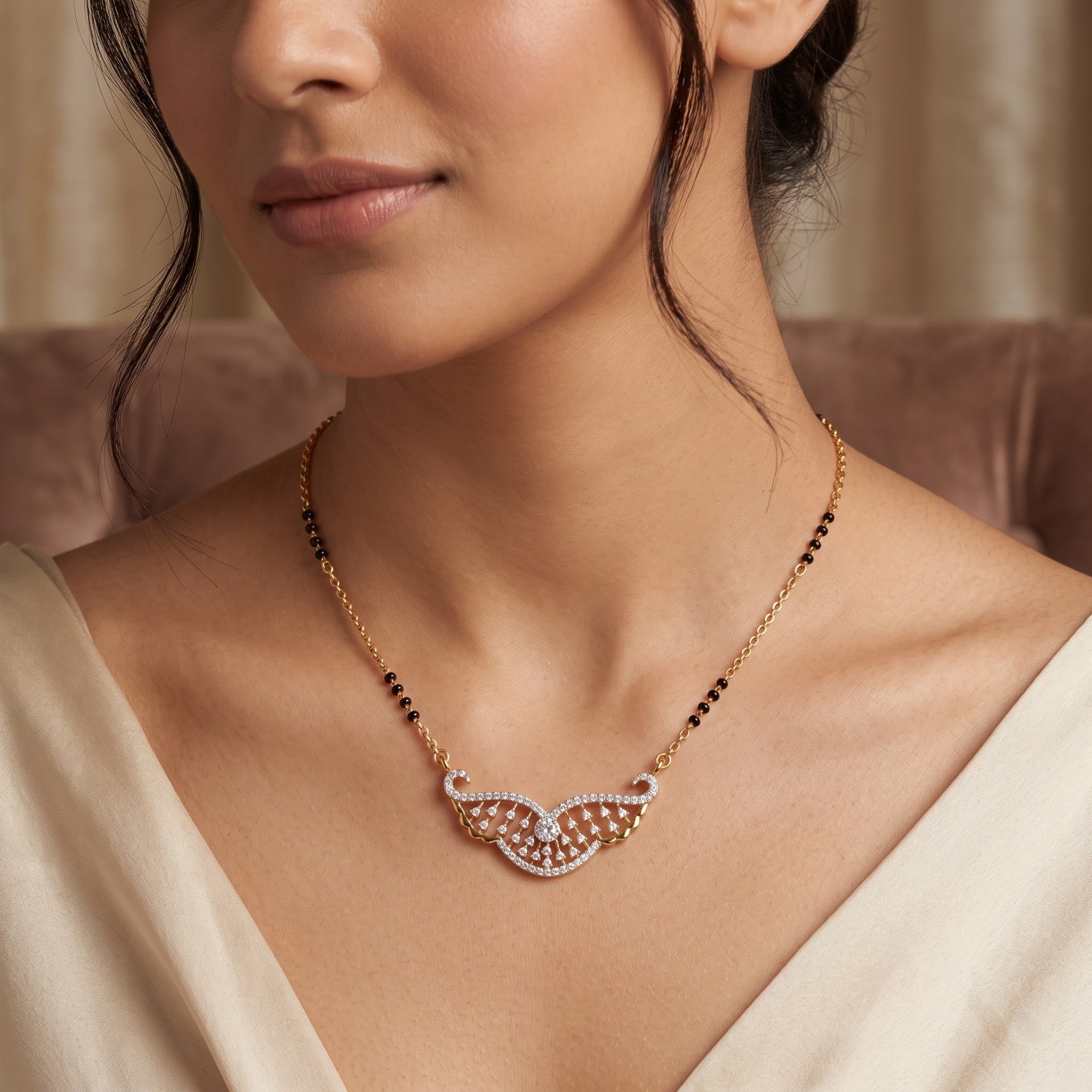 A close-up lifestyle shot of a model wearing a delicate gold chain necklace with a wing-shaped pendant adorned with small clear stones and black beads.