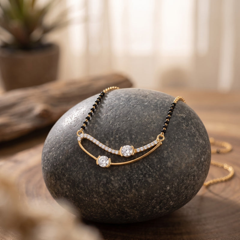 Gold necklace with three clear gemstones and a curved pavé detail, draped over a dark gray stone on a wooden surface.
