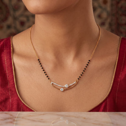 A close-up of a woman wearing a delicate gold necklace with a curved pavé center and black bead accents, paired with a deep red satin top.