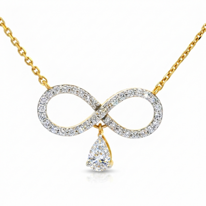 A gold necklace featuring an infinity symbol pendant paved with clear stones, with a teardrop-shaped clear gemstone hanging from the center, shown on a white background.