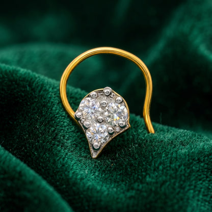 A gold hoop nosering with a leaf-shaped cluster of clear gemstones in a silver-toned setting, displayed on a textured dark green velvet surface.