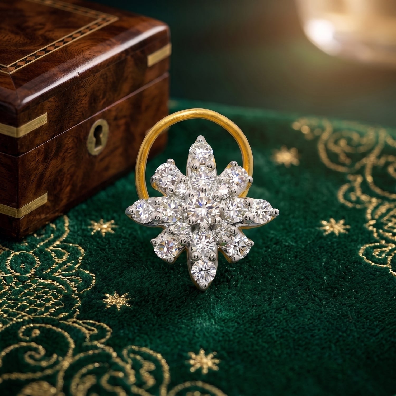 A gold and diamond snowflake-style nose ring displayed on a dark green embroidered fabric surface next to a wooden box.