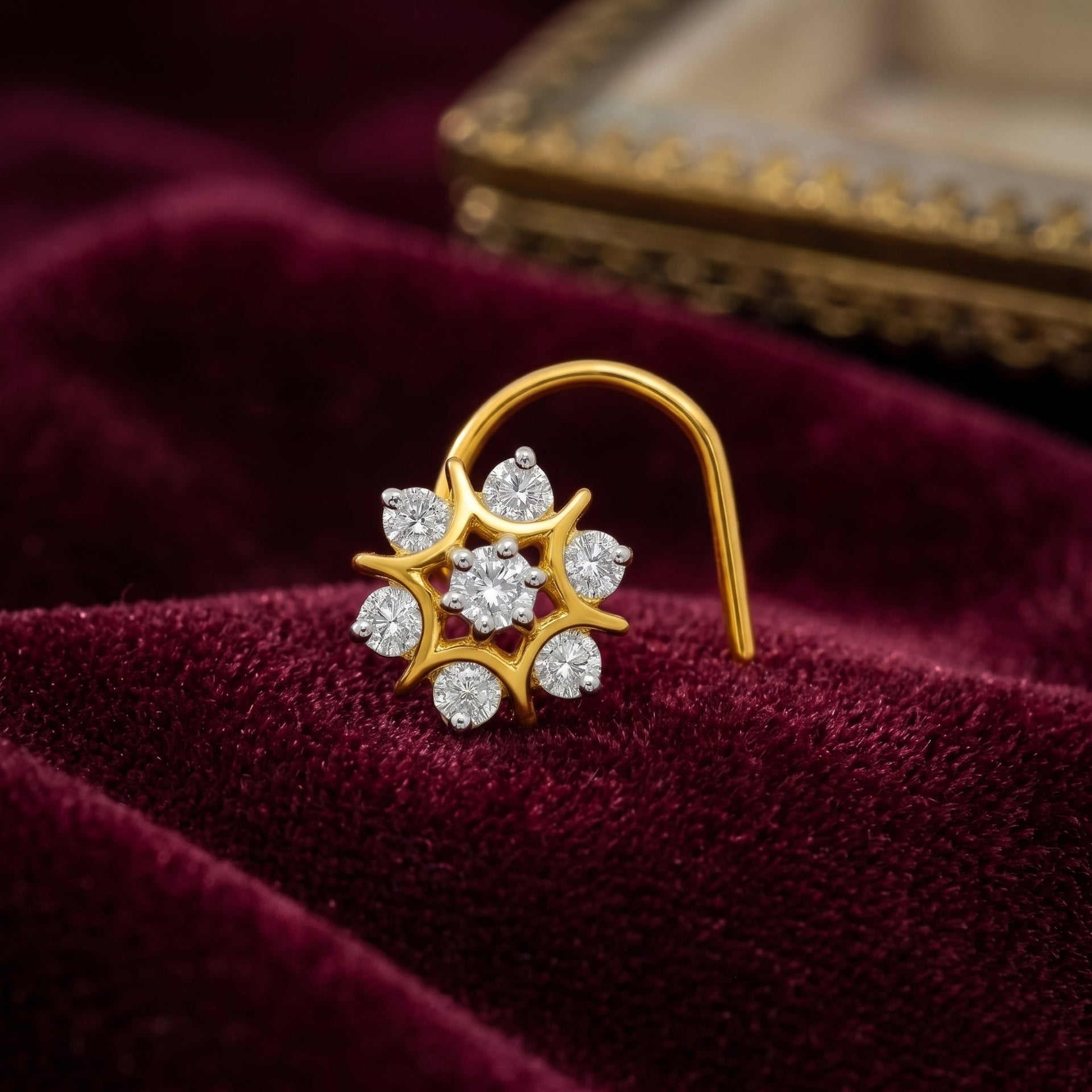 A gold crescent-shaped hoop nose ring with a flower cluster setting, featuring clear round-cut gemstones, displayed on a deep burgundy velvet surface.