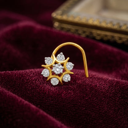 A gold crescent-shaped hoop nose ring with a flower cluster setting, featuring clear round-cut gemstones, displayed on a deep burgundy velvet surface.