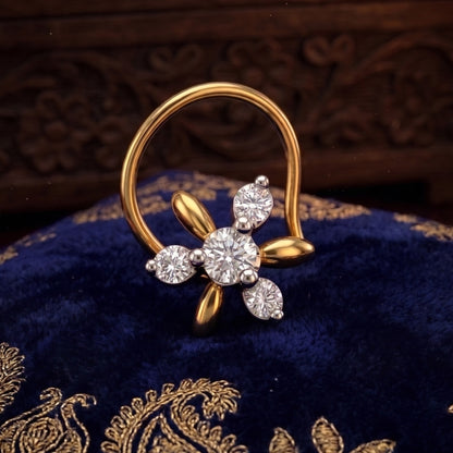 A gold and silver-tone flower-shaped nose ring with a large round center stone and three smaller accent stones, displayed on a dark blue velvet fabric with gold embroidery.