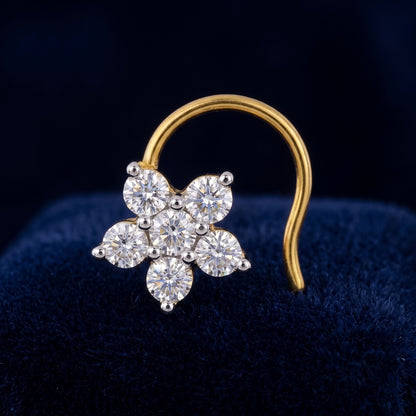 A gold nose ring featuring a flower-shaped cluster of clear round-cut gemstones, displayed on a dark blue velvet surface.