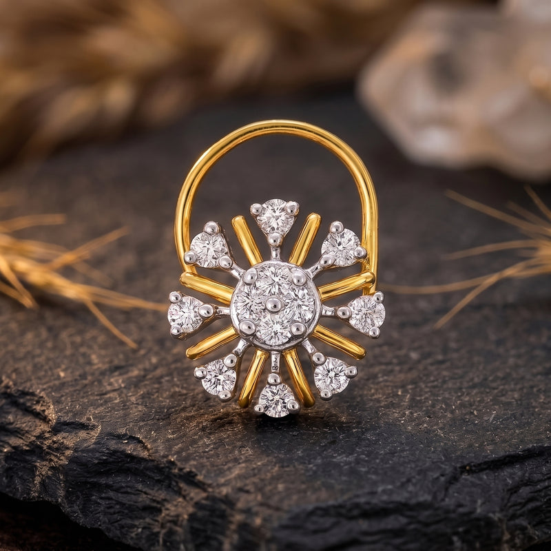 A gold and white gold sunburst ring with clear gemstones, displayed on a dark textured stone surface with dried grass and a blurred background.