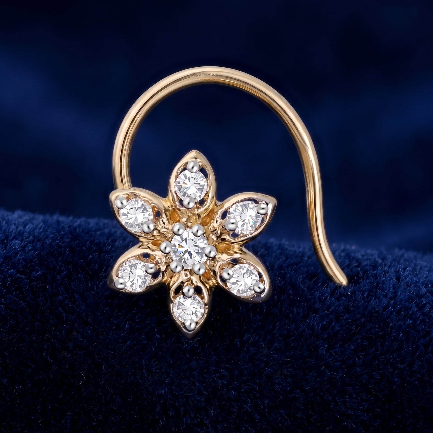 A gold flower-shaped earring with clear gemstones, displayed on a dark blue velvet surface.