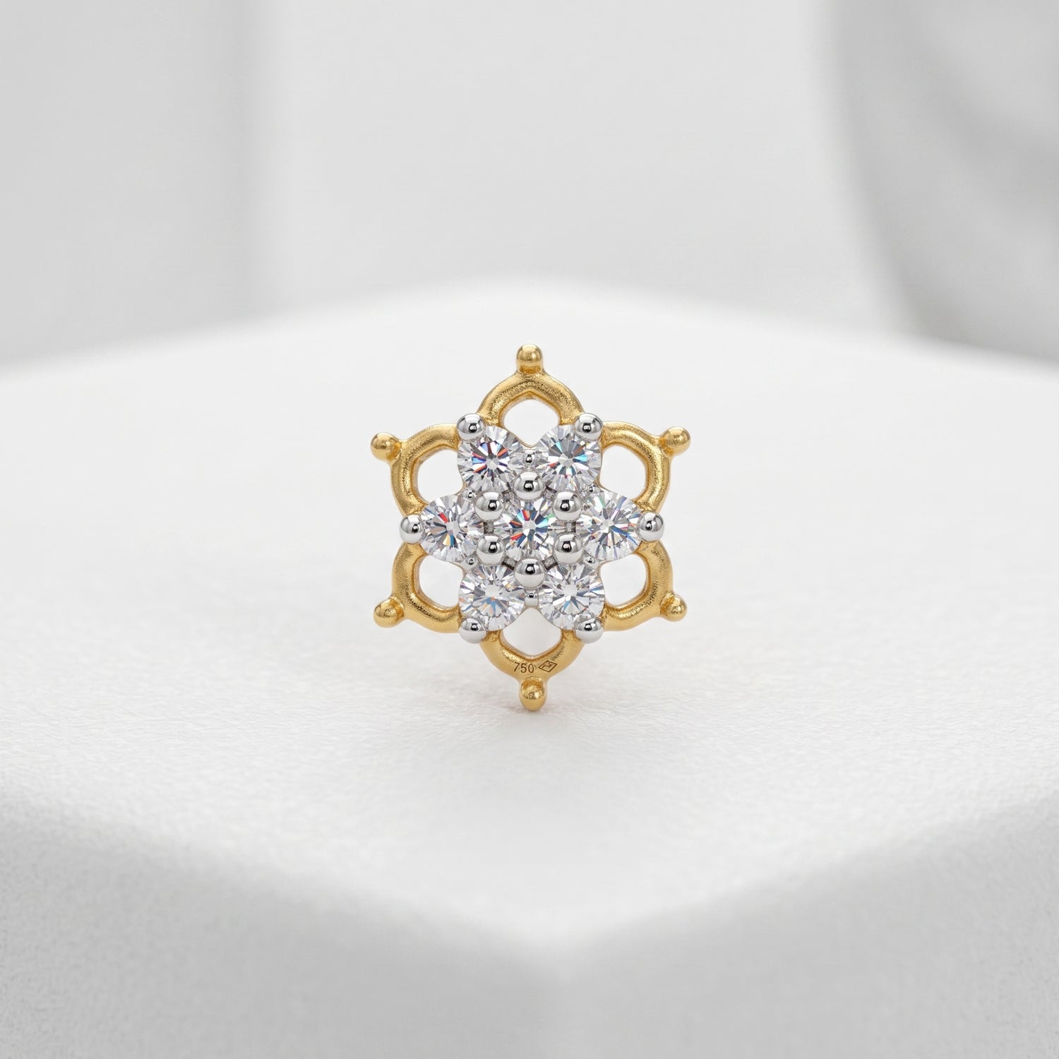 A gold ring with a multi-stone floral cluster center, displayed on a white textured surface.