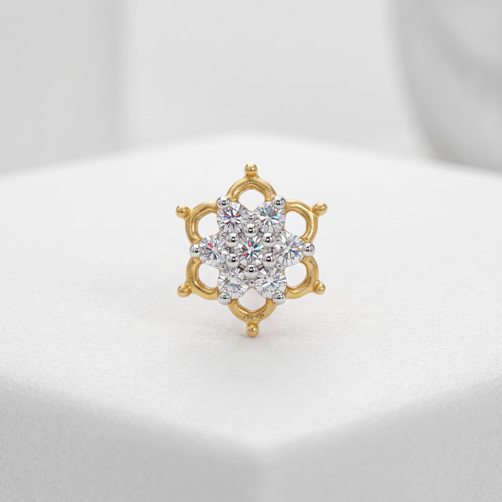 A gold ring with a multi-stone floral cluster center, displayed on a white textured surface.