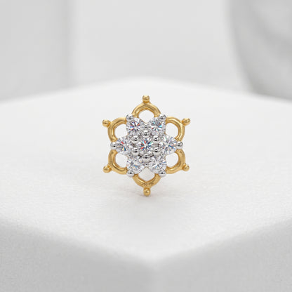 A gold ring with a multi-stone floral cluster center, displayed on a white textured surface.