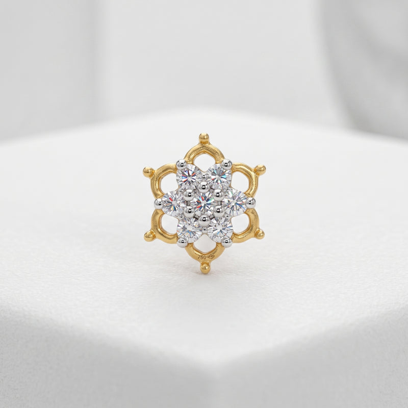 A gold ring with a multi-stone floral cluster center, displayed on a white textured surface.