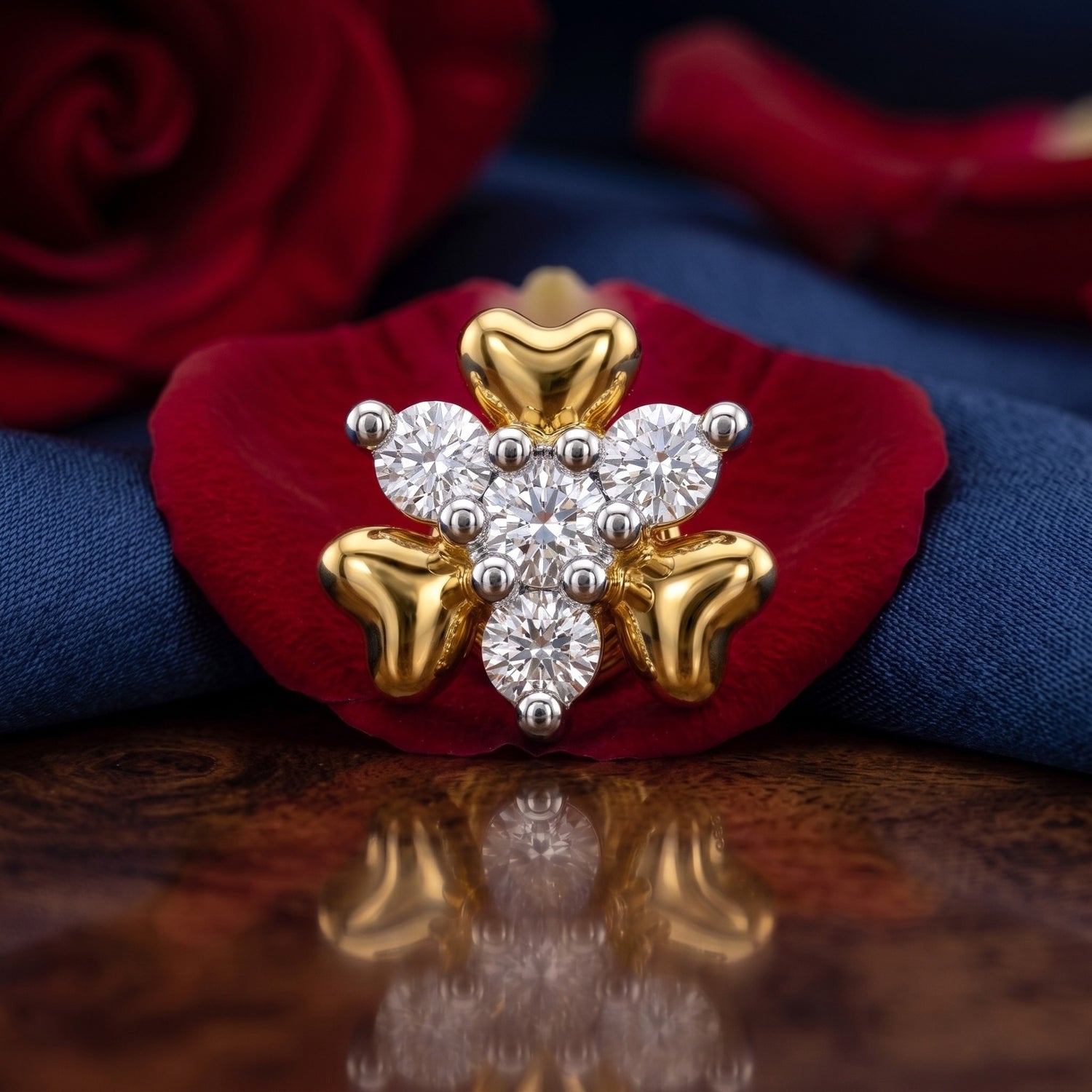 A gold and white diamond snowflake ring displayed on a red rose petal with a blue fabric background.